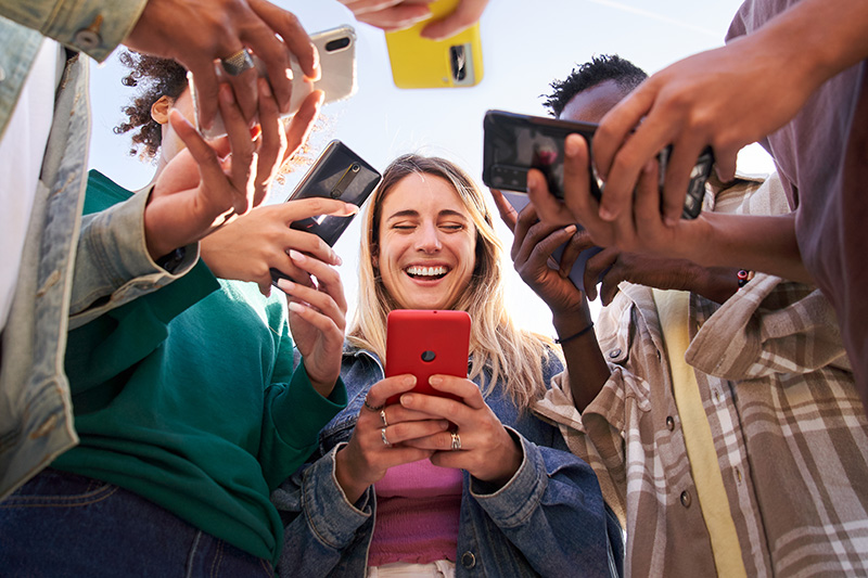 A group of teenagers stand in a circle looking at their phones.