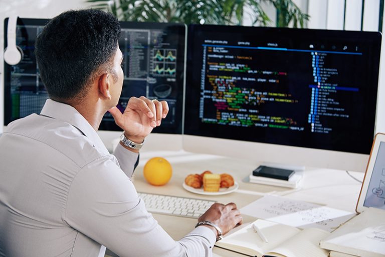 A developer sits infront of two large screens looking at code.