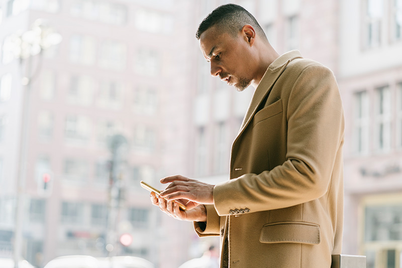 A twenty-year-old Turkish man stands outside looking at his phone.