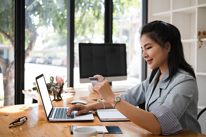 A woman looks at her credit card while making a purchase on her laptop.